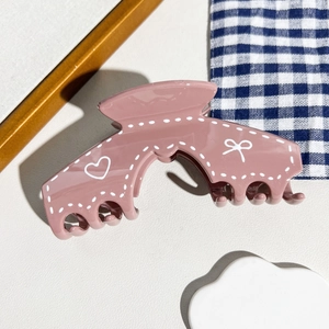 Détail d'une pince à cheveux rose crème avec motifs de cœurs et finition brillante