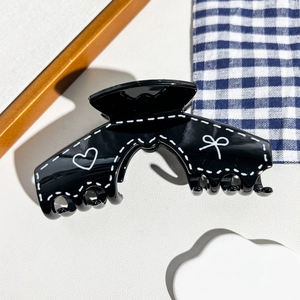 Détail d'une pince à cheveux noire avec motifs cœurs et nœuds sur plateau blanc