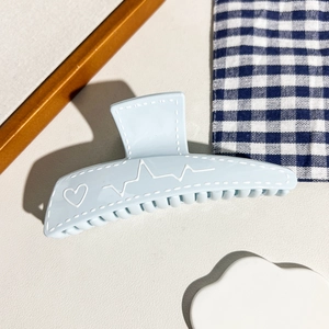 Détail d'une pince à cheveux mate bleu clair avec motif cœur blanc et lignes de pouls