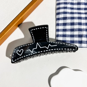 Détail d'une pince à cheveux noire brillante avec motifs de cœurs et lignes ECG