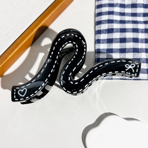 Détail d'une pince à cheveux noire ondulée avec motifs de cœurs et nœuds blancs