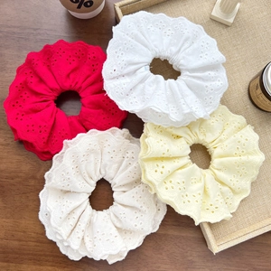 Close-up of four colors of delicate hollow embroidery lace scrunchies on a wooden tray