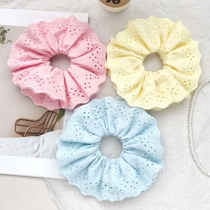 Detail of three eyelet lace scrunchies in pink, yellow, and blue with embroidery