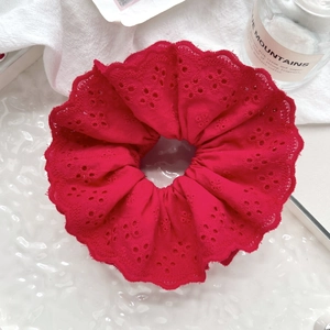 Close-up of red lace scrunchie with intricate hollow embroidery and floral texture