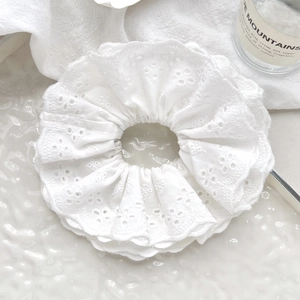 Detail shot of a white lace scrunchie with intricate embroidery on a minimalist background