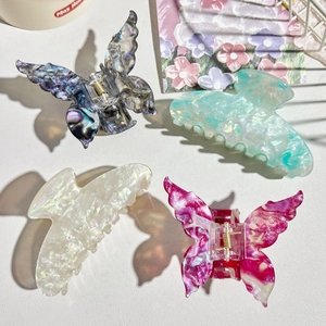 Flat lay of four iridescent acetate hair claws in butterfly and arched shapes on white leather