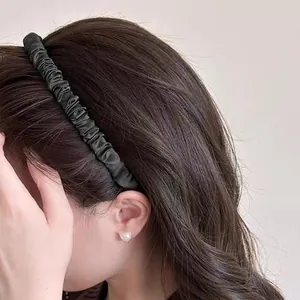 Elegant black pleated satin headband with a smooth silk texture shown on wavy brown hair