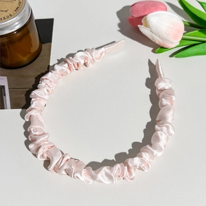 Close-up of light pink pleated satin headband placed on a minimalist desktop with flowers