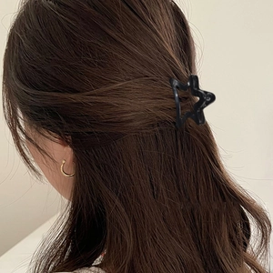 Pince à cheveux noire minimaliste en forme d'étoile sur des cheveux ondulés brun foncé