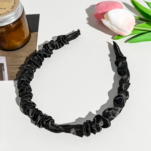 Detailed close-up of a black pleated satin scrunchie headband with silk-like glossy texture