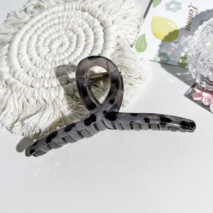 Macro detail of a large grey marble-patterned hair claw clip on a white leather surface