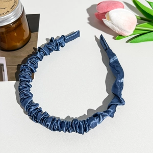 Detailed close-up of dark blue pleated satin headband with silky texture on white surface