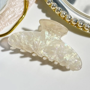Close-up of cream pearlescent hair claw clip with iridescent finish on mirror base
