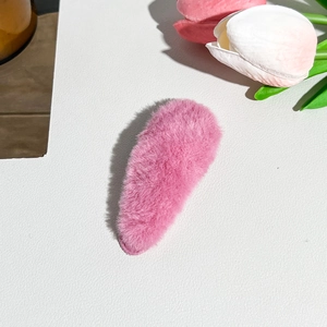 Close-up of a soft pink plush hair clip with a fluffy texture on a white surface