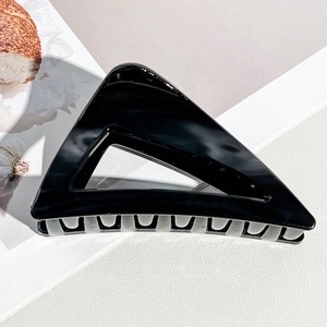 Détail de la pince à cheveux triangulaire noire brillante sur une surface en cuir