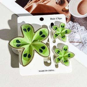 Detailed view of green kiwi-patterned flower hair clips on a white presentation card