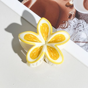 Detail of vibrant yellow flower claw clip with citrus patterns on a textured white background