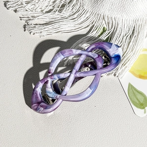 Detail view of purple marble pattern infinity knot spring clip on white textured surface