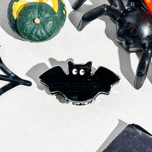 Close-up of a glossy black bat hair clip with a spooky Halloween pumpkin background