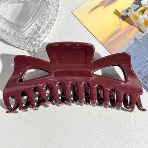 Close-up of a large deep red matte hair claw clip on a white leather texture surface
