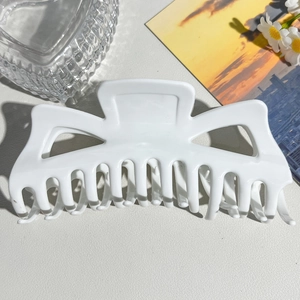 Top-down view of a large white matte shark hair claw clip styled on a lifestyle background