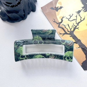 Close-up of Halloween hair claw clip with dark green skull pattern on white leather background