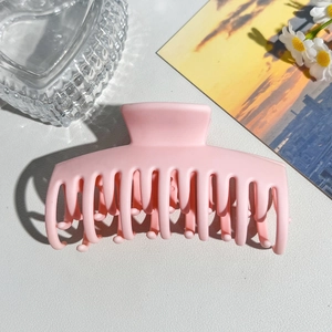 Pink matte hair claw clip shown on a white leather surface with aesthetic daisy decor
