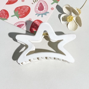 Detail of white hollow star hair claw clip with golden spring on textured background
