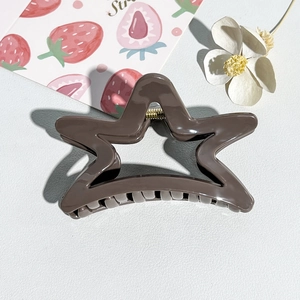 Close-up of star-shaped glossy brown hair claw clip with metal spring on decorative background