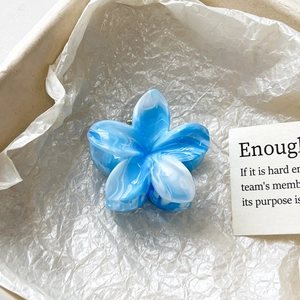Détail d'une pince à cheveux fleur marbrée bleue dans un emballage élégant