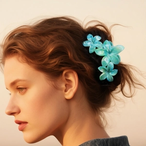 Pince à cheveux fleur de frangipanier marbrée bleu-vert portée par un modèle sous une lumière douce