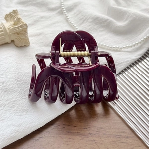 Detail view of large burgundy hair claw clip with golden metal spring on white fabric