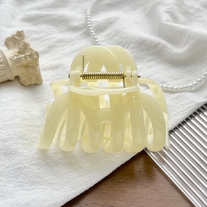 Detailed macro view of cream resin shark hair claw clip with golden metal spring