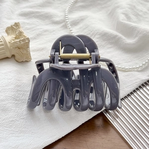 Detail view of a large grey hair claw clip with golden spring on textured fabric