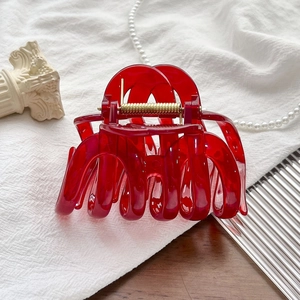 Detail of a large red resin hair claw clip with golden metal spring and cut-out design