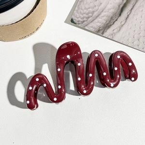 Détail d'une pince à cheveux ondulée rouge vin avec des motifs de pois blancs élégants