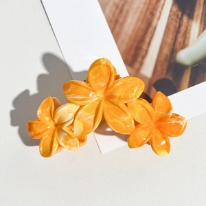 Détail d'une pince à cheveux fleur de frangipanier orange avec texture marbrée pour la plage