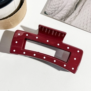 Détail d'une pince à cheveux rouge à pois blancs avec un design creux rectangulaire
