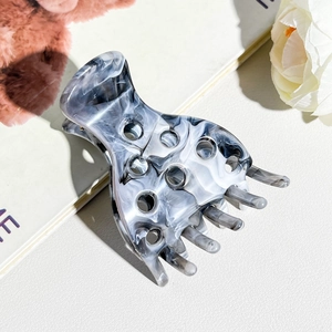 Close-up of marble pattern acetate hair claw clip with cutout design on book surface