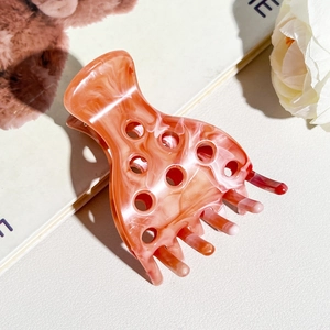 Close-up of orange-pink marble acetate hair claw clip with cutout design and thick teeth