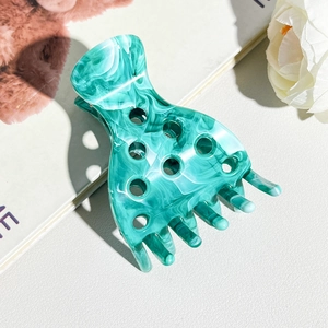 Detailed view of large marble texture green hair claw clip with cutout design on leather