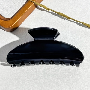 Detailed view of large glossy black hair claw clip on a textured white surface