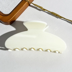 Close-up of a cream-white minimalist semi-circular hair claw clip on a textured surface