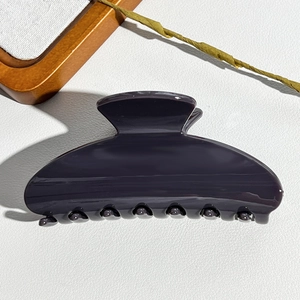 Close-up of a large glossy semicircular shark hair claw clip on a white leather surface
