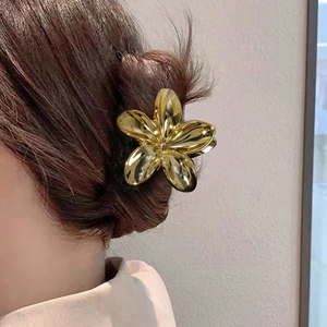 Pince à cheveux fleur de frangipanier dorée en métal sur une coiffure chignon élégante