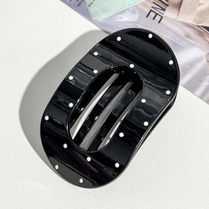 Detailed view of an oval black hair claw clip with white polka dots on textured surface