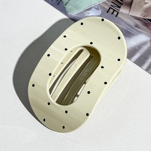 Close-up of a cream-colored oval hair claw clip with black polka dots and hollow center