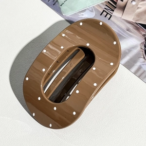Detail view of large caramel brown hair claw with white polka dots on glossy finish