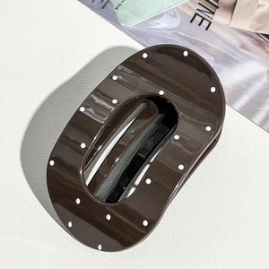 Macro detail of large brown polka dot hair claw clip with glossy finish on white surface