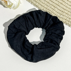 Detailed view of black textured fabric scrunchie with soft pleats on white leather background